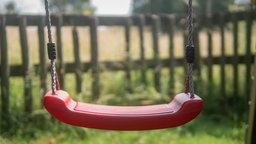 Eine leere, rote Schaukel in der Sonne