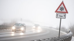 Auf einer befahrenen Straße warnt ein Schild vor Schnee- und Eisglätte