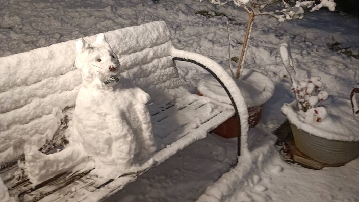 Eine aus Schnee gebaute Katze sitzt auf einer Bank