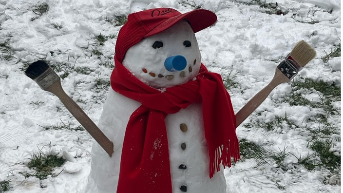 Ein Schneemann mit roter Cap, Schal und Armen aus Pinseln