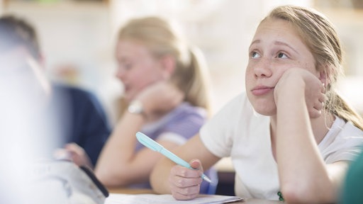 Mädchen in Schulklasse schaut nachdenklich nach oben