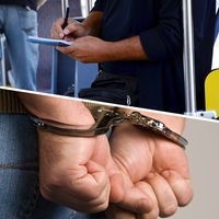 Ein Kontrolleur schreibt auf seinen Block und eine Person trägt Handschellen.