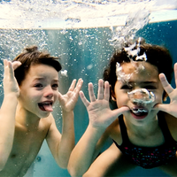 Zwei Kinder tauchen unter Wasser und schneiden fröhliche Grimassen