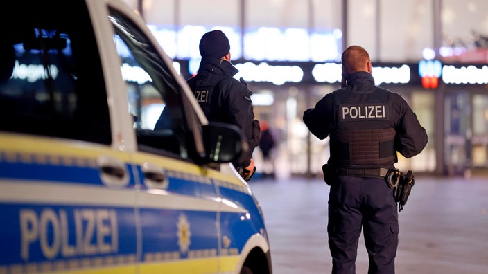 Zwei Polizisten stehen auf dem Bahnhofsvorplatz des Kölner Hauptbahnhofs. 