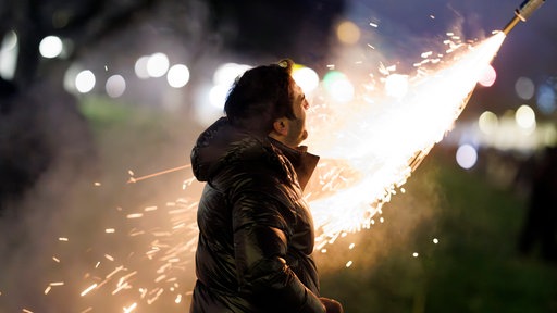 Ein Mann steht vor einer Silvesterrakete und schaut sich das Feuerwerk an.