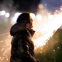 Ein Mann steht vor einer Silvesterrakete und schaut sich das Feuerwerk an.