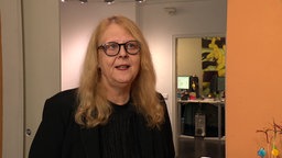 Eine ältere blonde Frau mit schwarzer runder Brille in einem Büro