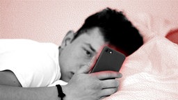 Ein Jugendlicher schaut im Bett auf sein Smartphone