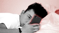 Ein Jugendlicher schaut im Bett auf sein Smartphone