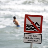 Schild "Nicht Baden - Gefährliche Strömung - Lebensgefahr!", Badegäste im Hintergrund