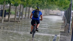 Ein Radfahrer fährt bei Gewitterregen am Rheinufer in Köln auf dem Fahrrad.