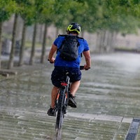 Ein Radfahrer fährt bei Gewitterregen am Rheinufer in Köln auf dem Fahrrad.