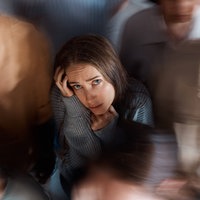 Symbolbild: Eine junge Frau steht mit ängstlichem Blick inmitten vieler Menchen.
