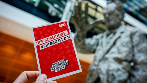 Flyer "Der Koalitionsvertrag ist da" vor Statue von Willy Brandt