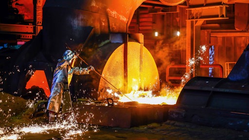 Arbeiter in Hitzeschutzkleidung bei der Arbeit an einem Hochofen in der Stahlindustrie, Funken sprühen