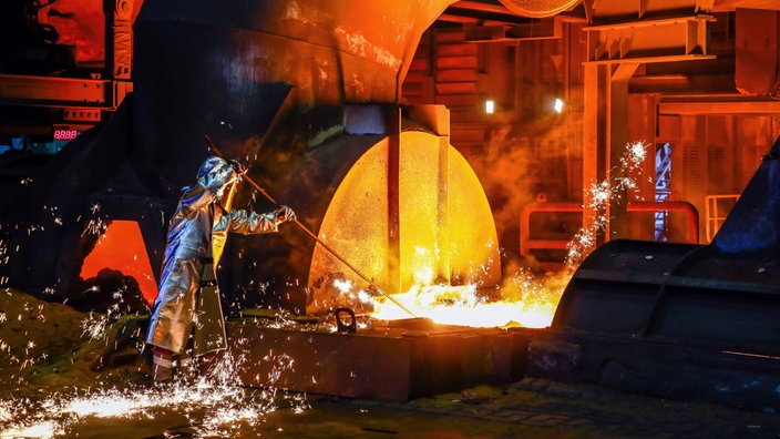 Arbeiter in Hitzeschutzkleidung bei der Arbeit an einem Hochofen in der Stahlindustrie, Funken sprühen