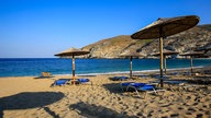 Sonnenliegen und -schirme am Strand Ormos Zorkou auf der Insel Andros in Griechenland
