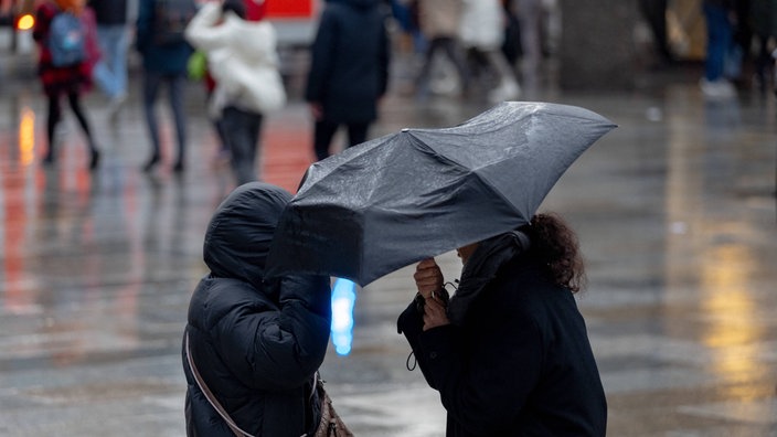 Passanten werden von Winböen gemischt mit Regen erfasst und strapaziert die Regenschirme