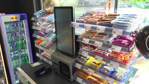 Eine Digitale Kasse umgeben von verschiedenen Schokoriegeln im Fröndenberger Supermarkt ohne Personal. Auf der linken Seite ein Kühlschrank mit koffeinhaltigen Getränken.