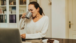 Eine Frau sitzt am Laptop und trinkt Kaffee