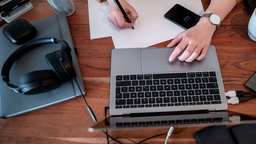 Eine Person arbeitet an einem Laptop und macht sich Notizen 