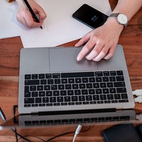 Eine Person arbeitet an einem Laptop und macht sich Notizen 