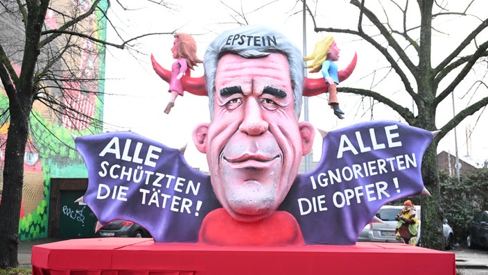 Ein riesiger Jeffrey Epstein-Kopf mit Teufelshörnern, die zwei Frauen aufspießen