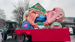 Donald Trump und Wladimir Putin essen ein blaues Schwein mit der Aufschrift "Europa"