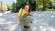 Eine Frau trinkt Wasser aus einem Trinkwasserspender