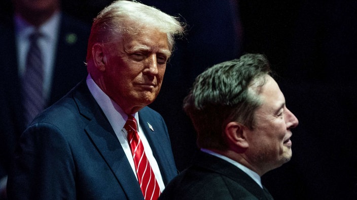 Das Bild zeigt Donald Trump und Elon Musk vor dunklem Hintergrund