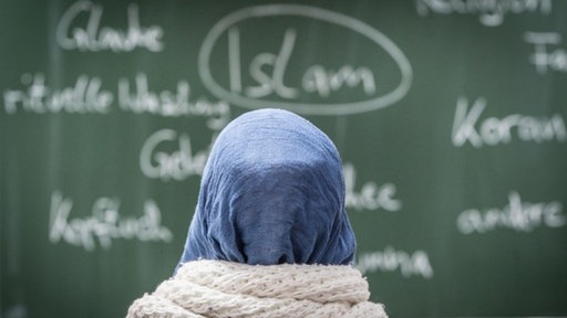 Ein Mädchen mit Kopftuch sitzt im islamischen Religionsunterricht in einer Schulklasse