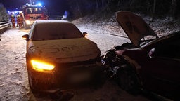 Zwei Autos stehen nach einem Unfall auf einer verschneiten Straße, im Hintergrund ist die Feuerwehr zu sehen