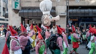 Kostümierte Zwerge halten einen großen Kopf mit Kochmütze hoch