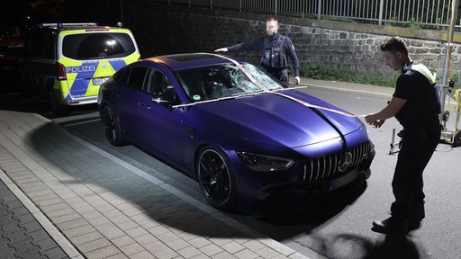 Ein beschädigter Mercedes AMG steht nach einem Unfall auf einer Straße in Remscheid Lennep. Polizeibeamte sichern Spuren an dem Fahrzeug.