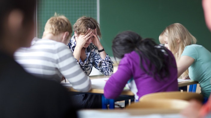 Überforderte Lehrerin sitzt mit Schülern in einem Klassenraum