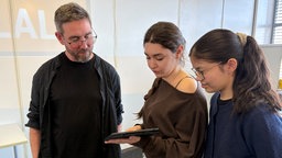 Zwei Schülerinnen zeigen dem Spieleentwickler Friedrich ihr Tablet