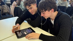 Zwei Schüler sitzen über einem Tablet