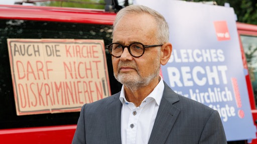 Gynäkologe Joachim Volz steht vor zwei Protestplakaten, die sich gegen das Verbot von Schwangerschaftsabbrüchen durch die Kirche aussprechen.
