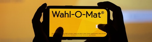 Zwei Hände halten ein Handy mit dem Wahl-O-Mat-Logo auf dem Bildschirm