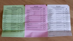 Drei Stimmzettel der Stadt Düsseldorf liegen nebeneinander auf einem Tisch. 