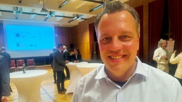 Sacha Reichelt, ein Mann im blauen Hemd, lächelt freundlich in die Kamera.