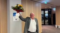 Das Bild zeigt Sebastian Schuster, der einen Blumenstrauß hochhält.