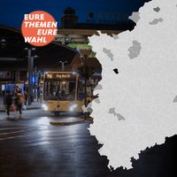 Ein Linienbus steht nachts an einer Bushaltestelle, im Vordergrung eine Karte mit den Gemeinde-Umrissen von NRW