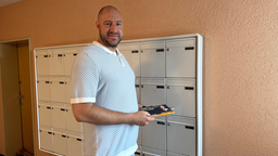 Das Bild zeigt einen Mann mit Wahlwerbung in der Hand vor einem Briefkasten