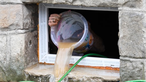 Ein Eimer Wasser wird aus einem Kellerfenster heraus entleert