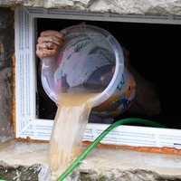 Ein Eimer Wasser wird aus einem Kellerfenster heraus entleert