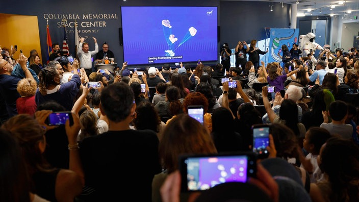 Im Columbia Memorial Space Center schauen Menschen die Live-Übertragung der Wasserlandung auf einer Leinwand