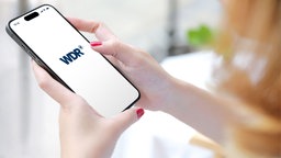 Eine Frau hat auf einem Smartphone die WDR aktuell App geöffnet.