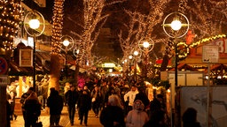 Menschen gehen unter Bäumen mit Lichterketten über den Weihnachtsmarkt in Dortmund.