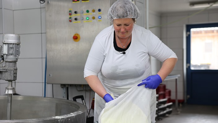 Eine Frau macht Frischkäse in der Produktionshalle.